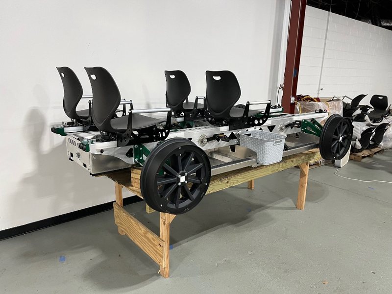 A green four-seat Rail Glider on a workshop bench, showing the industrial aluminum frame, plastic basket, and four flanged rail wheels.