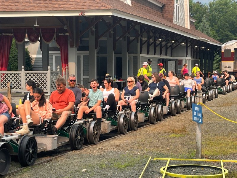 A group of green Rail Gliders on the rails at a station, with riders seated and ready to go out together.