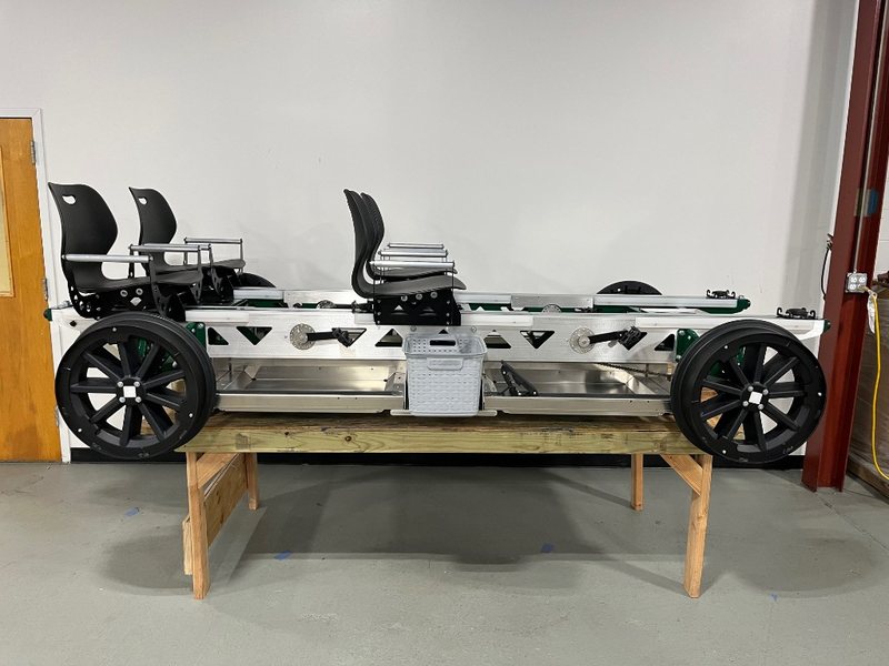 Side view of a green four-seat Rail Glider on a workshop bench, showing pedal cranks at each seat and the truss-style side rails.