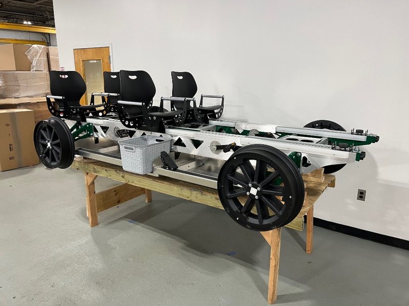 Three-quarter view of a green four-seat Rail Glider on a workshop bench, with black seats and flanged rail wheels.